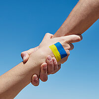 Lend a hand help painted in ukrainian flag colors against blue s Verbunden mit den Menschen in der Ukraine